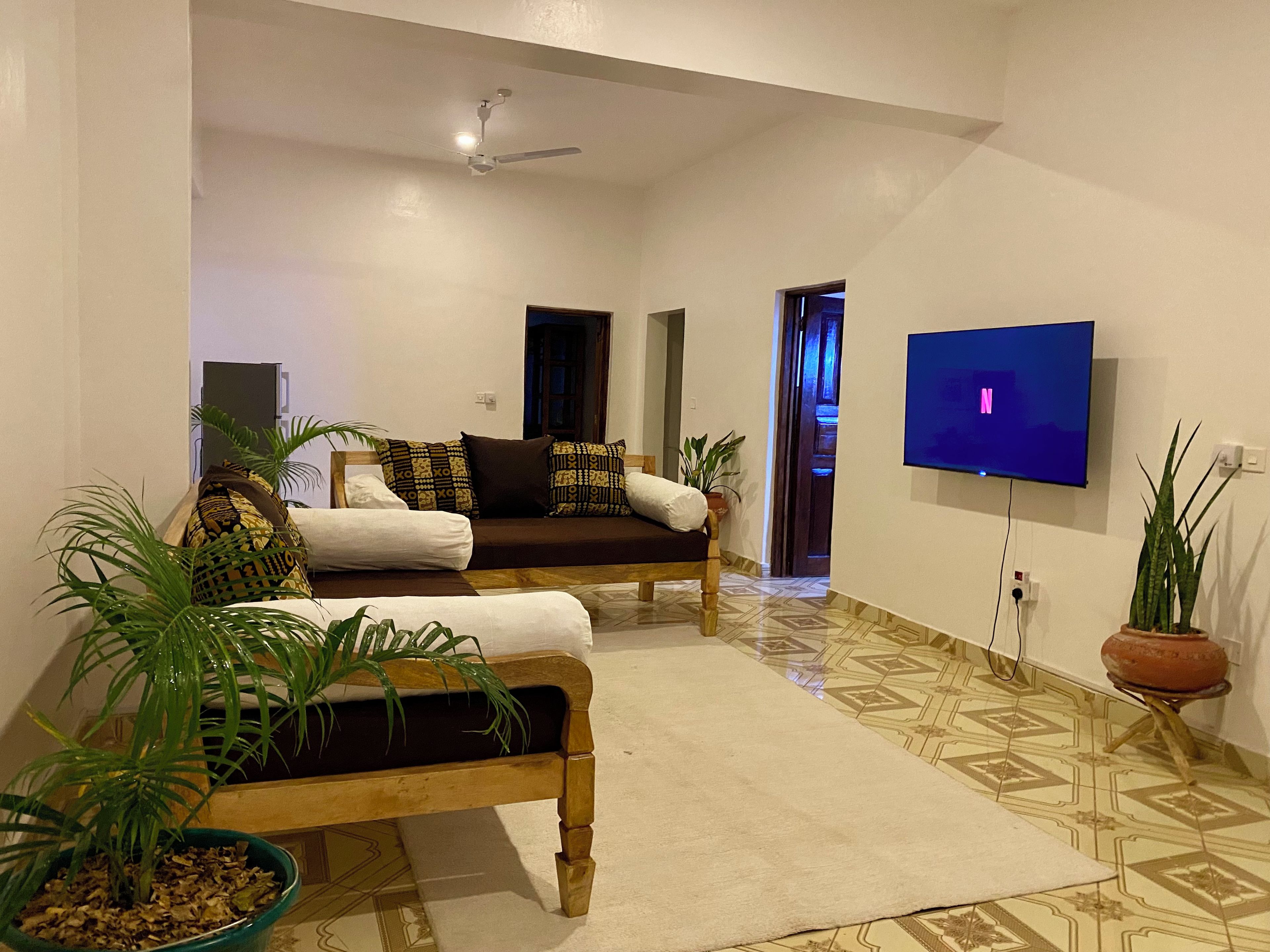 A living room with a sofa, a coffee table, a TV mounted on the wall, and a ceiling fan.