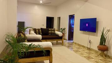 A living room with a sofa, a coffee table, a TV mounted on the wall, and a ceiling fan.