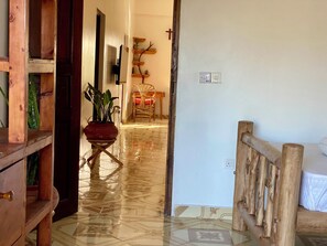 Un couloir avec un banc en bois, une plante en pot, une chaise et une étagère fixée au mur, ornée d’objets décoratifs.
