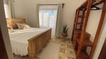 A bedroom with a wooden bed, a potted plant, and a wooden shelf unit.