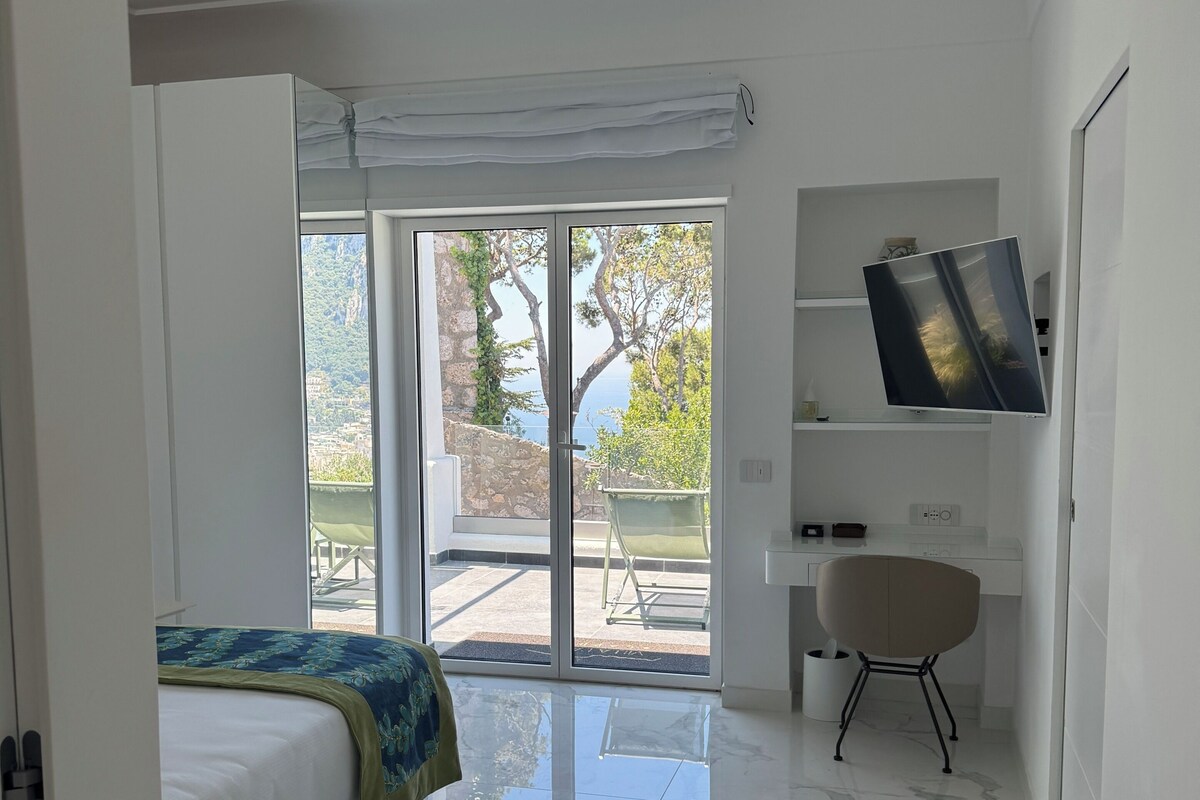 A modern bedroom with a bed, a desk, and a chair. There is a sliding glass door leading to an outdoor area.