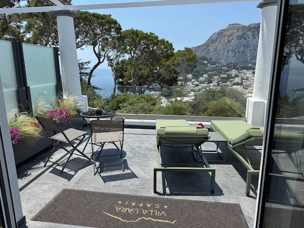 A balcony with a view of the sea, a table, chairs, and a small garden area.