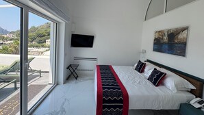 A hotel room with a bed, a TV, a painting, and a view of a coastal area. - Villa L'Ara Due (Capri)