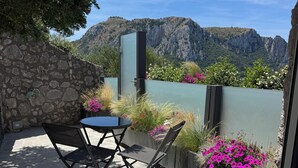 A patio with a table and chairs, a stone wall, and a view of mountains. - Villa L'Ara Due (Capri)