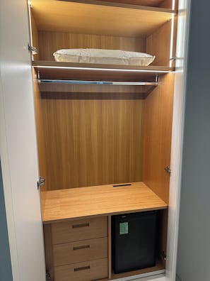 A walk-in closet with wooden doors, a hanging rod, and a small black appliance.