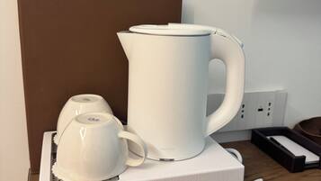 A white kettle and a white mug on a white tray, placed on a wooden table with a brown headboard in the background.