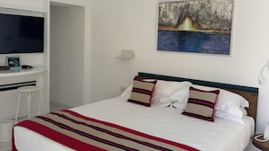 A hotel room with a bed, a desk with a flat-screen TV, a painting on the wall, and a telephone on the nightstand. - Villa L'Ara Due (Capri)