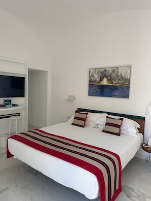 A hotel room with a bed, a desk with a flat-screen TV, a painting on the wall, and a telephone on the nightstand. - Villa L'Ara Due (Capri)
