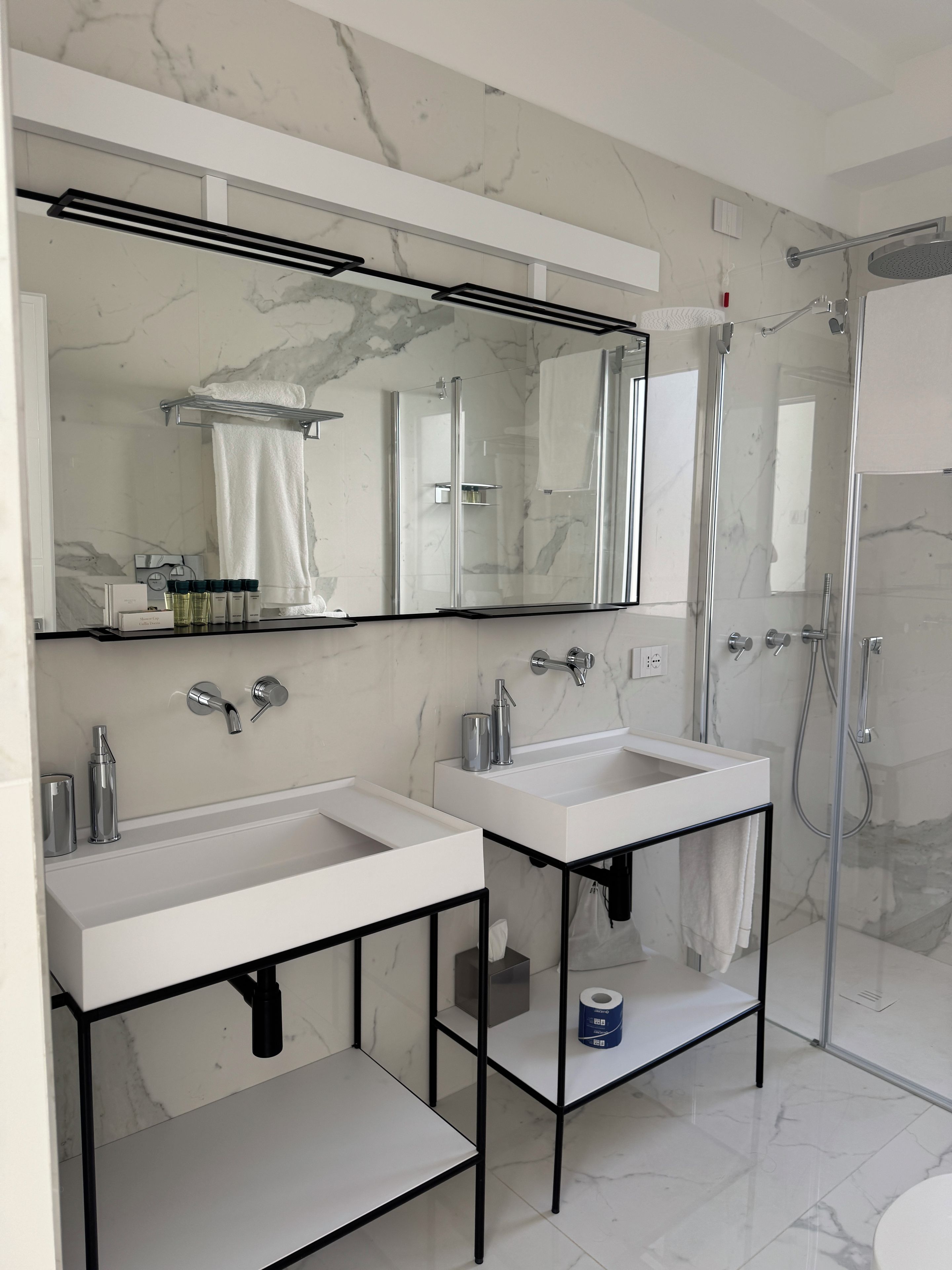 Un baño moderno con dos lavamanos, un espejo grande y una ducha con mampara de vidrio.