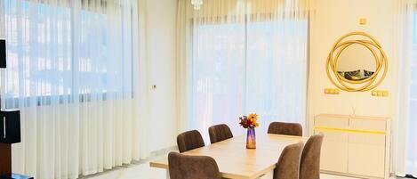 Un coin repas avec une table ronde, six chaises et un lustre.