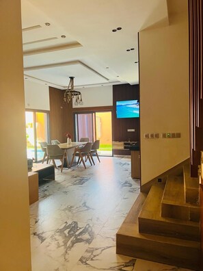 Un interior moderno con una zona de comedor, un televisor montado en la pared y una escalera.