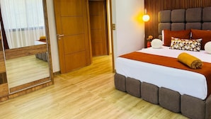 Hotellihuone, jossa on suuri sänky, peili, puinen vaatekaappi ja seinään kiinnitetty valaisin.