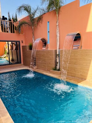 A swimming pool with two water features, a wooden deck, and a view of a building with a balcony. - 🏡Anaya Villa — private pool, elegance, and absolute comfort. (Igui N'Targuit taghazout)