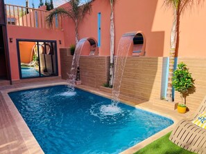 A swimming pool with two water features, a wooden deck, and a small plant. - Vrbo Property (Igui N'Targuit taghazout)