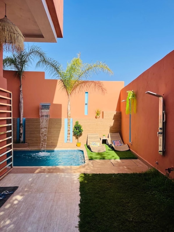 A pool area with a water feature, lounge chairs, and a small staircase leading to a door. - Vrbo Property (Igui N'Targuit taghazout)