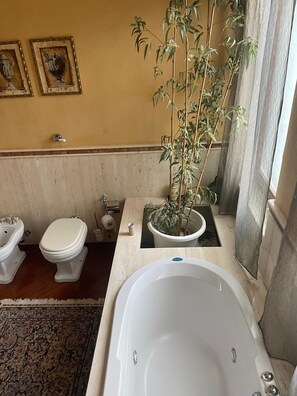 A bathroom with a bathtub, two toilets, a sink, and a potted plant. - Vrbo Property (borgetto)