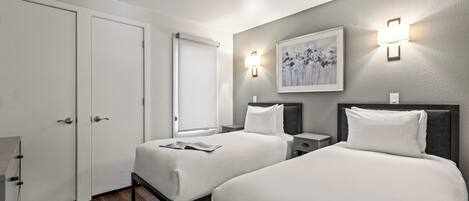 A hotel room with two beds, a nightstand, a wall-mounted light, and a door.