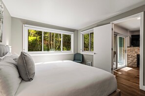 Een slaapkamer met een groot bed, twee ramen, een stoel en een deur naar een andere kamer.