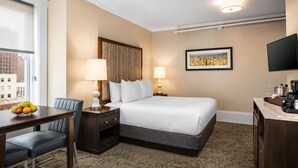 A hotel room with a bed, bedside tables, a desk with a chair, a fruit bowl, and a city view. - 1-Bedroom Hotel Suite in Historical San Francisco, close to AI Conference (San Francisco)