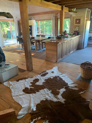 A spacious living area with a wooden floor, a large cowhide rug, a dining table, and a kitchen area with a bar.