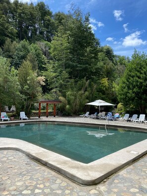 A swimming pool with lounge chairs and a gazebo surrounded by trees. - Vrbo Property (Pucon)