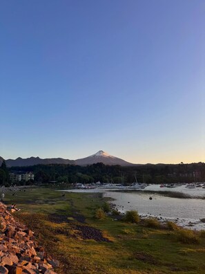 A coastal landscape with a mountain in the background, a marina with boats, and a grassy area with rocks.