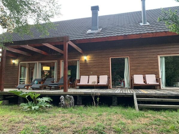 A wooden cabin with a covered deck, outdoor seating, and large windows.