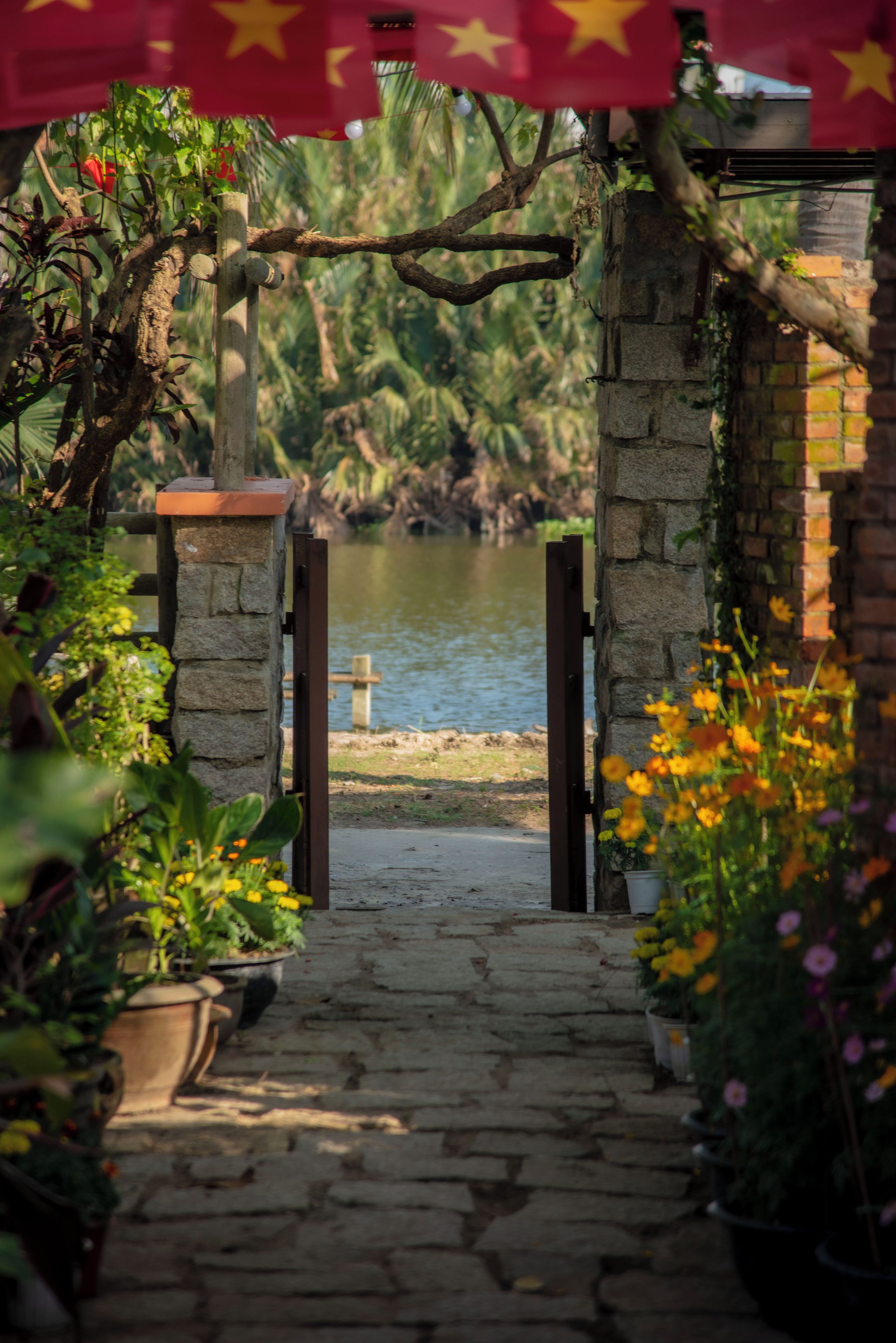 A stone pathway leading to a body of water, surrounded by potted plants and a brick wall.