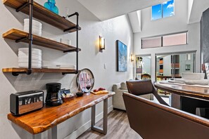 A modern kitchen with wooden shelves, a coffee maker, and a dining area with a view. - Across Stree from Ski Resort Base | Hot Tub | Managed by Park City Lodging (Park City)