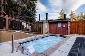 Ein Whirlpool mit Holzterrasse, einer Metallleiter und einem roten Gebäude im Hintergrund.