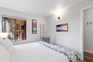 Ein Hotelzimmer mit Bett, Fenster mit Blick auf ein Gebäude, einer Wandleuchte und zwei gerahmten Bildern.