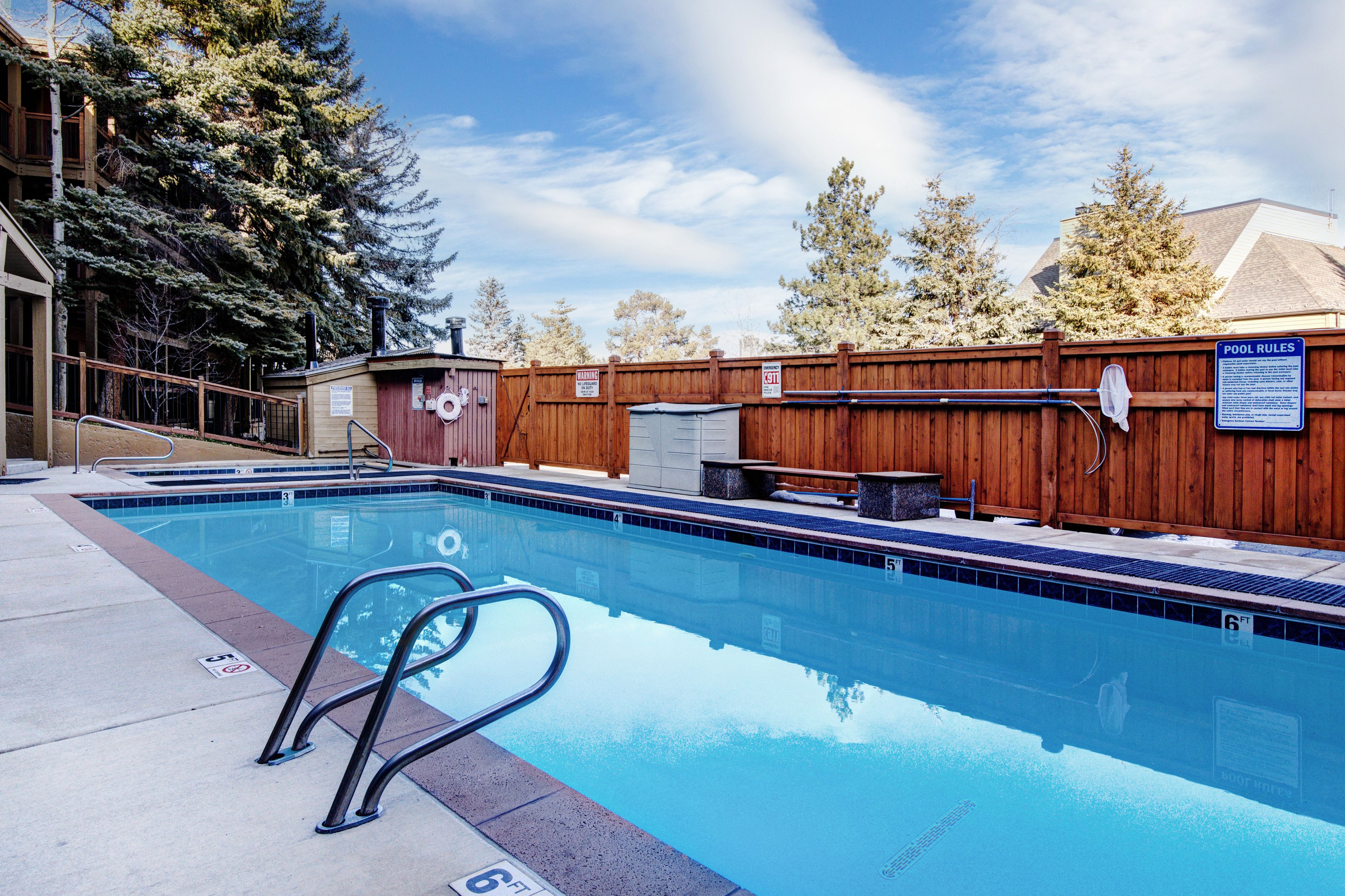 A swimming pool with a wooden fence, lifeguard stand, and a sign indicating pool rules.