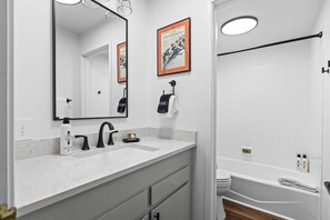 Een moderne badkamer met een witte wastafel, een grote spiegel, een badkuip en een toilet.