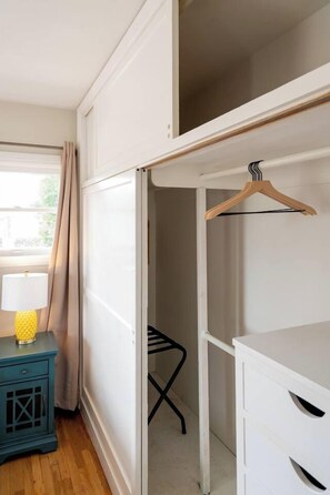 A room with a white wardrobe, a wooden hanger, a blue nightstand with a lamp, and a window with curtains. - Balboa park Craftsman home (San Diego)