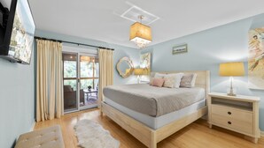 A bedroom with a bed, bedside tables, a TV, and a view through a sliding glass door. - Seabrook Exclusives | 1161 Summerwind (Seabrook Island)