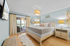 Een slaapkamer met een bed, nachtkastjes, een televisie en uitzicht door een schuifdeur.