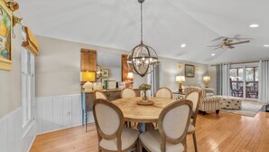 A dining area with a round table, chairs, and a chandelier. There is a ceiling fan and a view of the outdoors through a glass door. - Seabrook Exclusives | 1161 Summerwind (Seabrook Island)