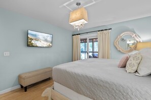 Ein Schlafzimmer mit einem Bett, einer Bank, einem Fernseher, einer Chandelier und Blick ins Freie.