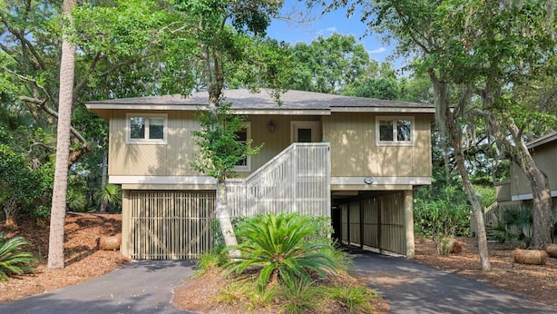 A two-story house with a covered garage, a front entrance with a staircase, and a driveway. - Seabrook Exclusives | 1161 Summerwind (Seabrook Island)