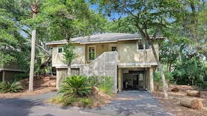 A two-story house with a covered porch, a driveway, and surrounding trees. - Seabrook Exclusives | 1161 Summerwind (Seabrook Island)