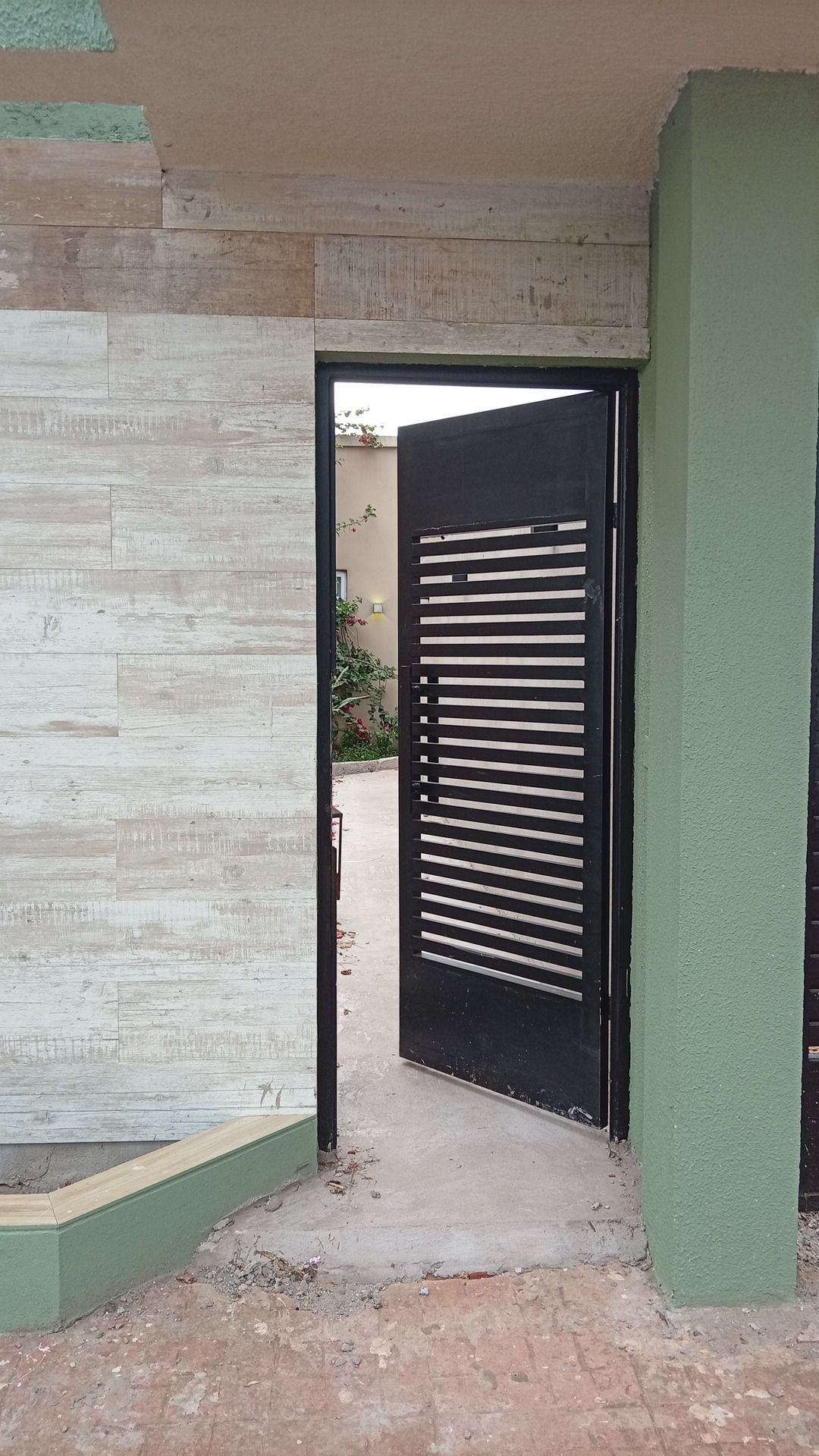 Een deuropening met een zwart metalen hekwerk, een betonnen vloer en een groene muur.