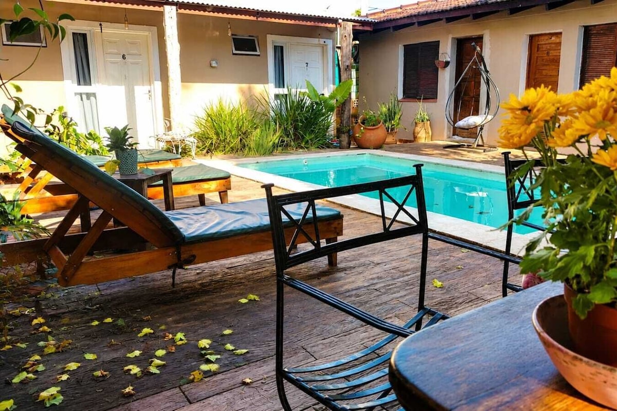 Zona junto a la piscina con piscina, sillas de descanso y una mesa con planta en maceta.