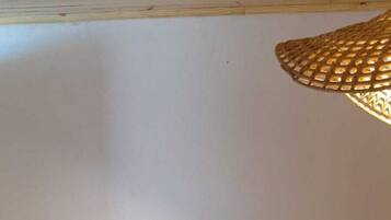A room with a bed, two wicker chairs, a small table with a tray, and a woven light fixture.