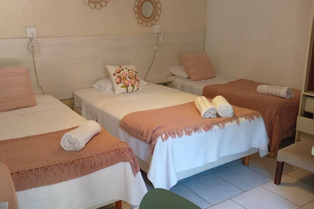 Habitación de hotel con tres camas, cada una con una almohada y una toalla enrollada.
