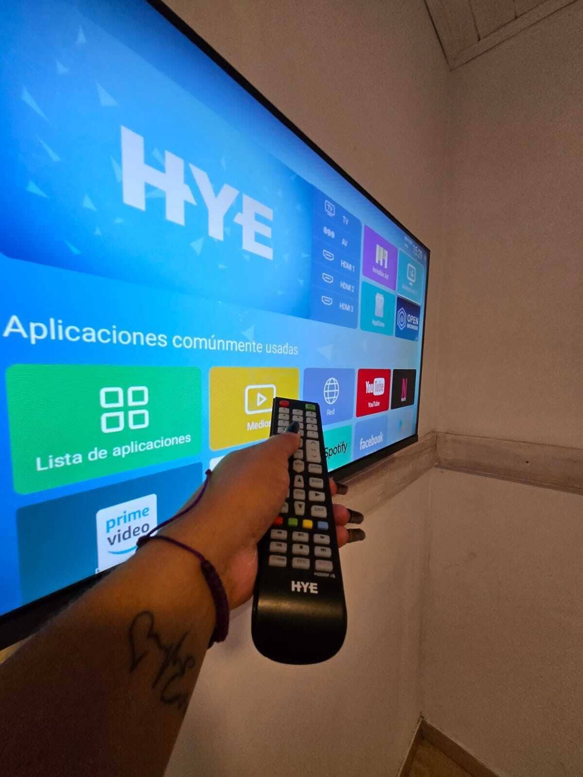 A hand holding a remote control in front of a television displaying a user interface with various application icons.
