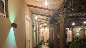 A covered outdoor corridor with a bench, potted plants, and a door at the end.