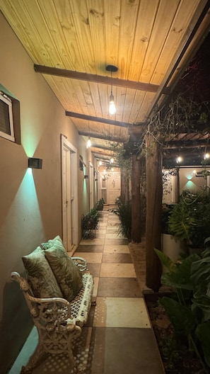 Un pasillo exterior cubierto con un banco, plantas en macetas y una puerta al final.