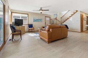 Ein geräumiges Wohnzimmer mit einem Ledersofa, einem Fernseher und einer Treppe, die zu einer anderen Ebene führt.