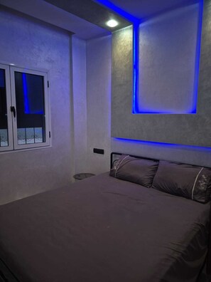 A bedroom with a bed, a window, and a wall with blue LED lighting. - Family Apartment (Agadir)