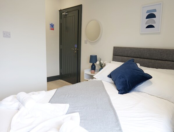 Habitación de hotel con cama, mesita de noche con lámpara, espejo y puerta con letrero.